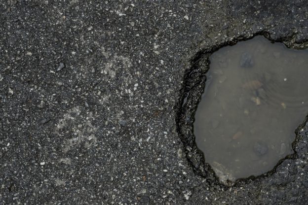 An asphalt parking lot with a pothole that has filled with water.