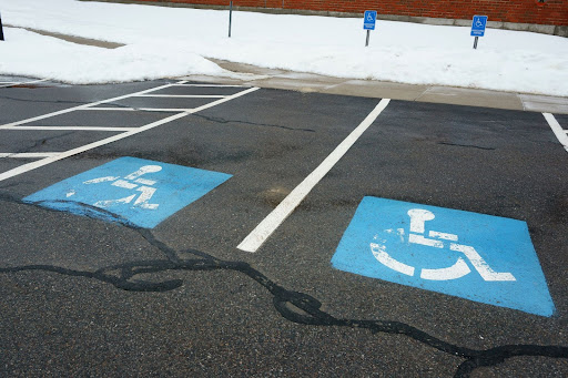 A parking lot with spots reserved for people with disabilities and asphalt cracks that have been filled in.