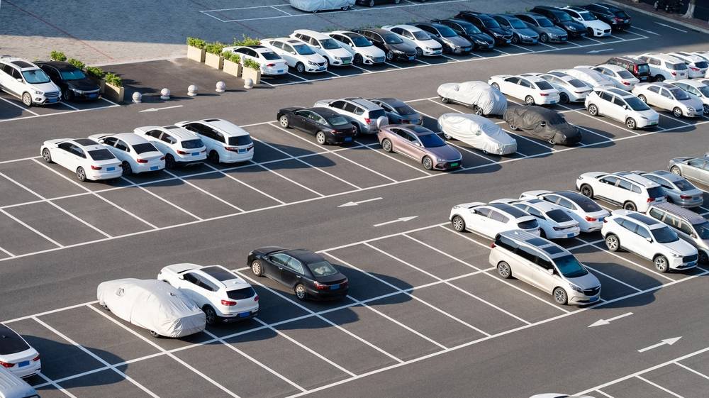 Spacious asphalt parking lot filled with neatly parked cars, featuring clear white line striping and directional arrows for organized traffic flow.
