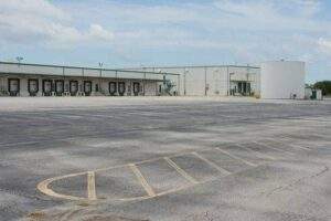 Large warehouse and distribution center with an expansive asphalt loading area, illustrating the heavy-duty pavement required to withstand frequent truck traffic and industrial operations.