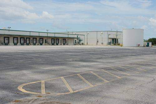 Large warehouse and distribution center with an expansive asphalt loading area, illustrating the heavy-duty pavement required to withstand frequent truck traffic and industrial operations.