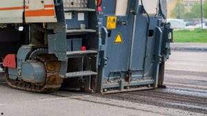 Cold milling machine grinding down top layer of damaged asphalt pavement during fall parking lot resurfacing