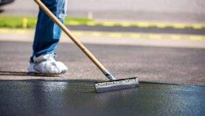 Maintenance worker using a squeegee to apply liquid sealant for asphalt crack sealing on a commercial parking lot